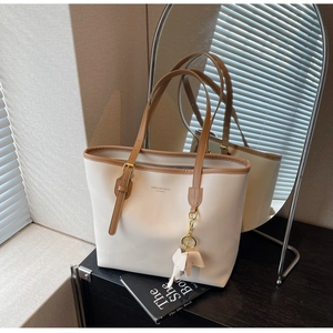Detail of off-white tote bag with brown leather trim and cute white elephant charm accessory
