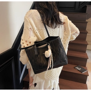Detail of large black tote bag with textured crinkle fabric and plush bear charm on shoulder