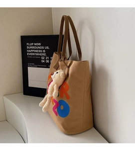 Detail of canvas tote bag with colorful logo and cute white plush bear charm