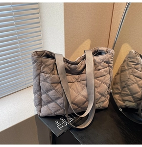 Detail of grey quilted tote bag with diamond stitching and woven handles in soft natural light