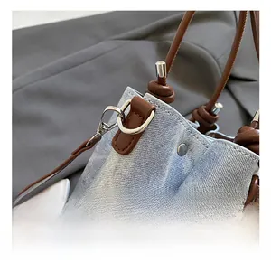Detail of silver metal hook connecting brown leather strap to blue denim bucket bag