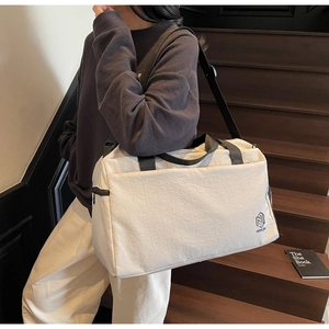 Detail view of large cream travel bag featuring side zipper pocket and brand logo