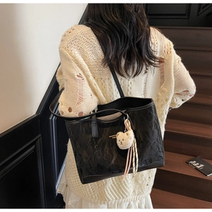 Detail of black pleated tote bag with plush bear charm and brand lettering