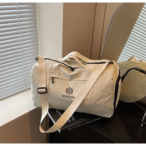 Detailed close-up of a cream-colored travel bag with dual handles and logo in soft studio light