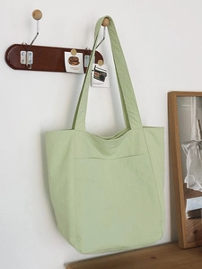 Minimalist green canvas tote bag with front pocket shown hanging on a wooden hook