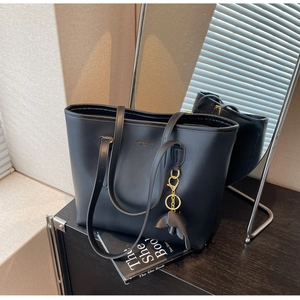 Detail of black leather tote bag featuring a gold elephant charm and minimalist brand logo