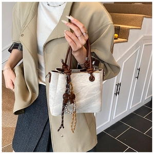 Detail of off-white bucket bag with brown rope handle and bow charm on beige trench coat