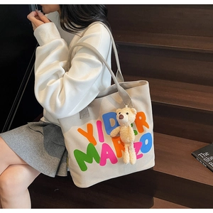 Detail of canvas tote bag with colorful YIDER MARZO lettering and plush bear charm