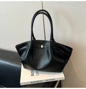 Detail of black pebbled leather tote bag with elegant pleats and golden square metal buckle