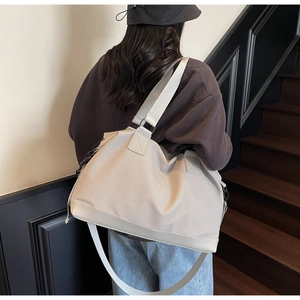 Detail of a large cream travel tote bag with mesh texture and reinforced leather bottom