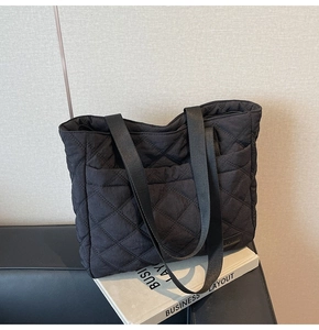 Close-up of black quilted tote bag with diamond pattern, side pocket and brand tag