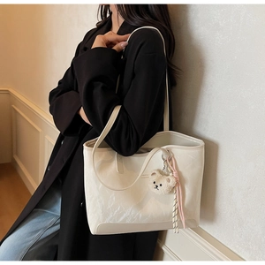 Detail of off-white tote bag with cloud texture, plush bear charm and long straps