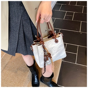 Detail of grey vintage bucket bag with brown cylindrical handle and ribbon charm