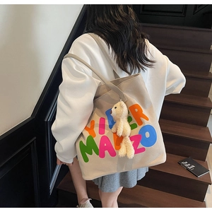 Detail of canvas tote bag with colorful letters and a cute plush bear pendant