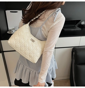 Side view of beige quilted shoulder bag with silver chain strap and metal swivel lock