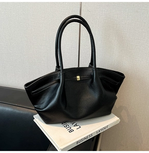 Detail of black pebbled leather tote bag with gold metal buckle on business books