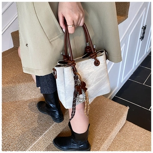 Detail view of cream fabric bucket bag featuring brown rope handle and bow accent