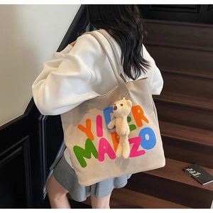 Detail of the cream canvas tote bag with colorful letters and a cute plush bear pendant