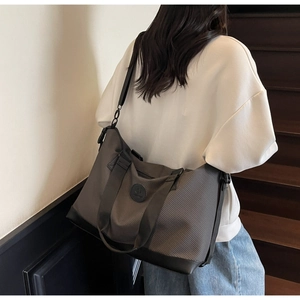 Detail of grey striped travel tote featuring leather logo patch and durable black base
