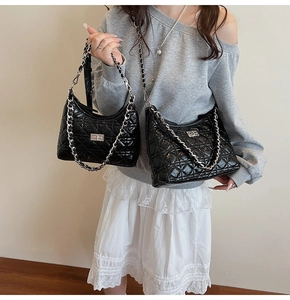 Detail of black quilted patent leather bucket bag with silver chain and metal clasp