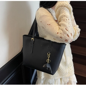 Classic black leather tote bag with gold hardware and leaf charm shown in lifestyle setting