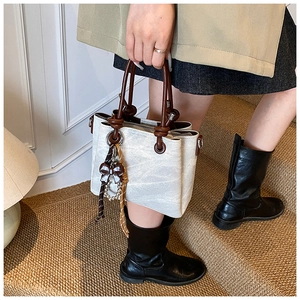 Detail of cream textured bucket bag with dark brown circular handle and elegant knot design