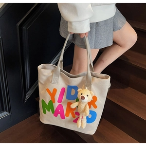 Detail of beige canvas tote bag with colorful letters and teddy bear charm on model