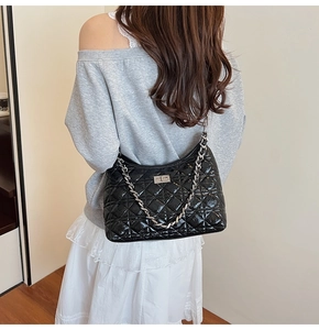 Detail of black quilted chain shoulder bag with glossy finish on a female model