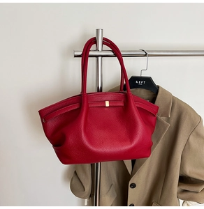 Detail of red leather tote bag with gold buckle hanging against a white wall background
