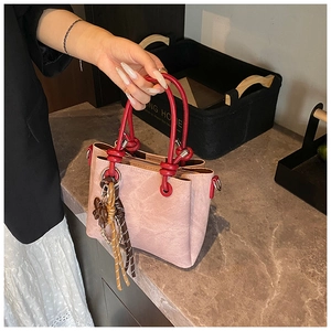Detail of pink matte tote with red knotted handle and floral tassel on stone surface