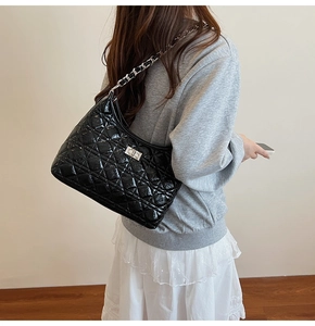Quilted black patent leather shoulder bag with silver chain strap shown on model's side