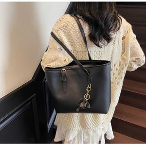 Detail of black tote bag with leather flower charm and adjustable gold buckle strap