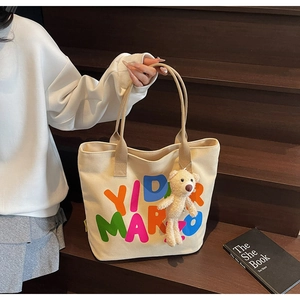Close-up of off-white canvas tote with YID MARZO lettering and a cute plush bear charm