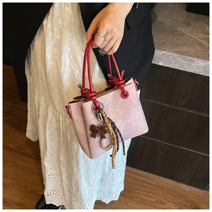 Detail of pink vintage bucket bag with red round handle and bow charm on white dress