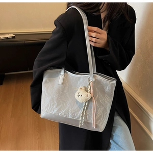 Detail of silver metallic tote bag with pleated texture and cute teddy bear charm
