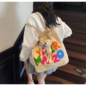 Detailed close-up of a beige canvas tote bag with colorful letters and a cute bear charm