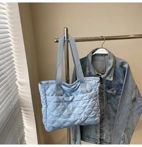 Close-up of light blue quilted tote bag with diamond stitching and woven handle on a hanger