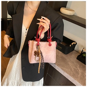 Pink crossbody bucket bag with contrast red handle and a brown decorative bow detail