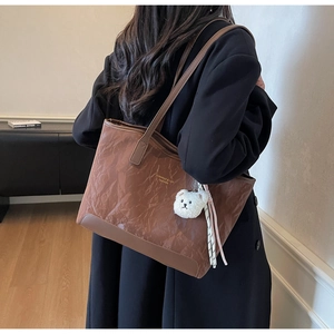 Brown tote bag with crinkle texture and white bear plush charm shown on shoulder