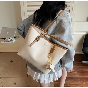 Detail of a large cream tote bag with brown trim and elephant charm worn over the shoulder
