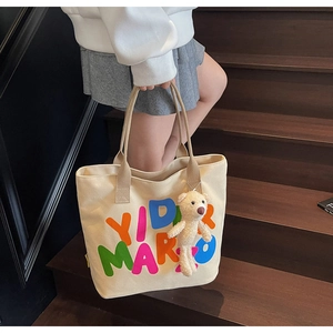 Detail of canvas tote bag with colorful letters and a cute plush bear charm on handles