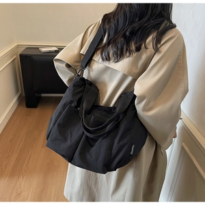 Detail of a large black nylon tote bag with wide strap and logo tag shown on model