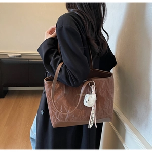 Close-up of pleated brown tote bag with cute bear charm and striped ribbon detail