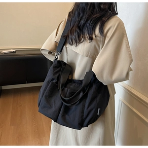 Detail of a large black nylon tote bag with side brand tag and adjustable strap