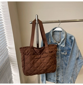 Detail of brown quilted nylon tote bag with front pocket and leather logo tag