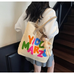 Detail of canvas tote bag featuring colorful letter prints and a plush bear pendant