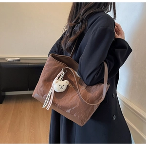 Detail of coffee brown pleated tote bag with plush bear charm and brand lettering