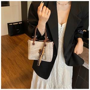 Detail of vintage beige bucket bag with braided brown handles and decorative tassels