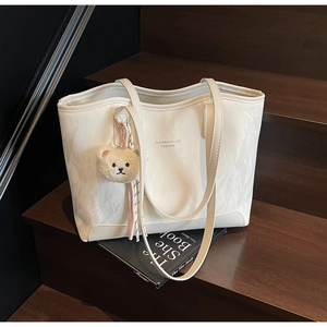 Detail of white tote bag with natural texture, plush bear charm and ribbon on stairs
