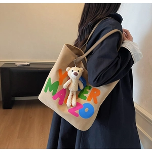 Khaki canvas tote bag with colorful letters and teddy bear charm on model shoulder